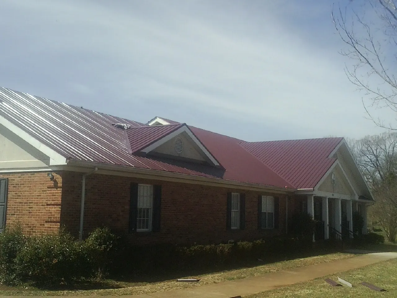 Red metal roof with gabled entries on a long brick building, from a Hail Damage Roof Repair job in Charlestown